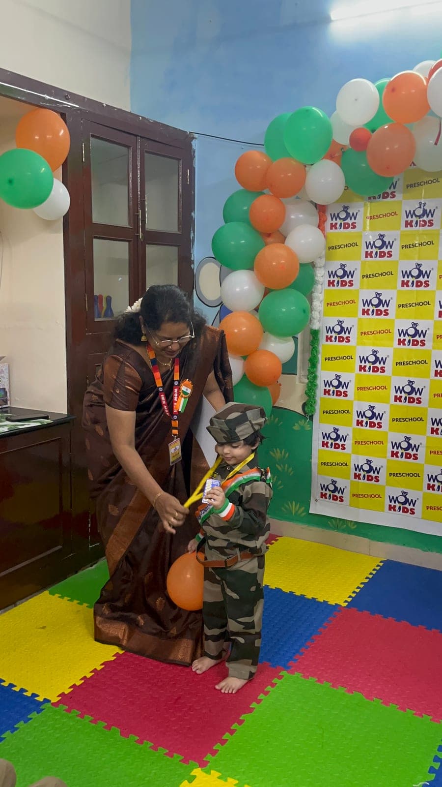 Teacher helping a toddler dressed as an army officer during the Independence Day celebration