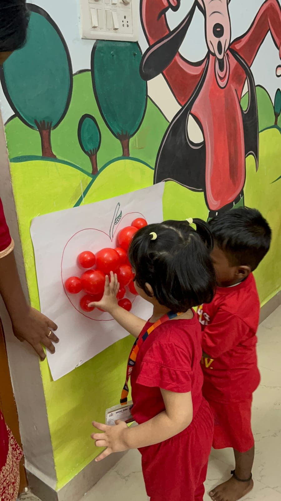 Two preschoolers working together to fill a paper apple with red balls on Red Day
